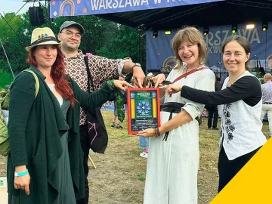 Cztery osoby z ekipy ogrodu trzymają dyplom konkursu Warszawa w Kwiatach na plenerowej scenie